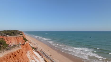 Praia-da-falesia-coastline-as-tourists-and-locals-wander-explore,-drone