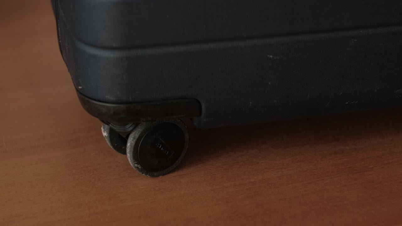 Primer plano de la rueda de una maleta rodando sobre suelo de madera