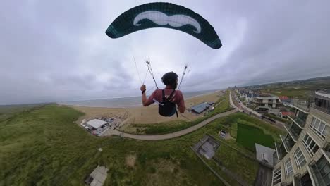 Back-FPV-view-of-paraglider-soaring-over-Dutch-residential-coastal-neighborhood