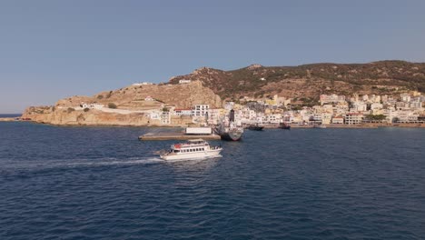 Drone follows a tourist boat arriving at Pigadia port, Karpathos, capturing the vibrant seafront and lively harbor atmosphere under bright sunny skies