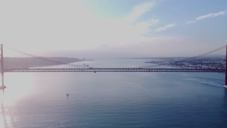 Vuelo-A-Gran-Altura-Sobre-El-Puente-Parecido-A-La-Puerta-Dorada-En-Portugal-Sobre-El-Río-Tejo-Filmado-Bajo-El-Sol-Brillante