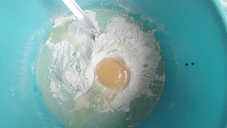 homemade baking dropping egg into sticky raw cake batter mixture in blue bowl