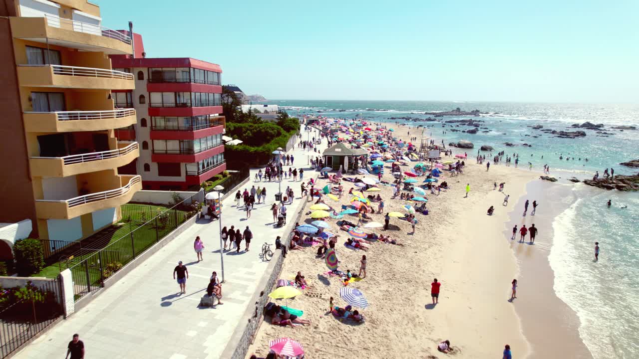 drone vuela sobre la playa de pejerrey con personas disfrutando de los últimos días de verano con edificios para el turismo, algarrobo, chile