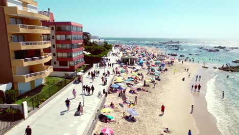 Drohnenflug-über-Den-Strand-Von-Pejerrey-Mit-Menschen,-Die-Die-Letzten-Sommertage-Mit-Gebäuden-Für-Den-Tourismus,-Algarrobo,-Chile-Genießen