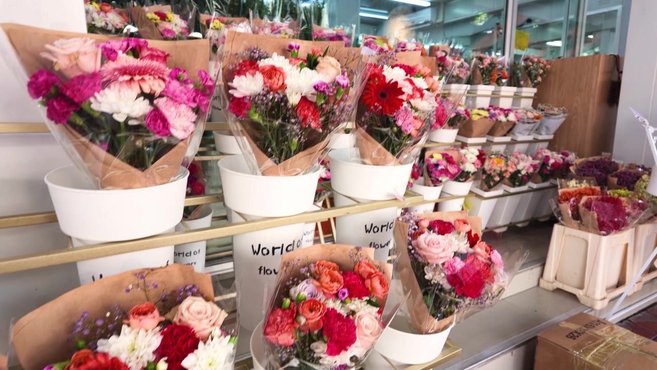 Levende blomsterarrangementer med roser og nelliker står i hvide spande på et marked.