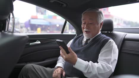 4k asian senior businessman sitting on car back seat using mobile phone video conference with business partner