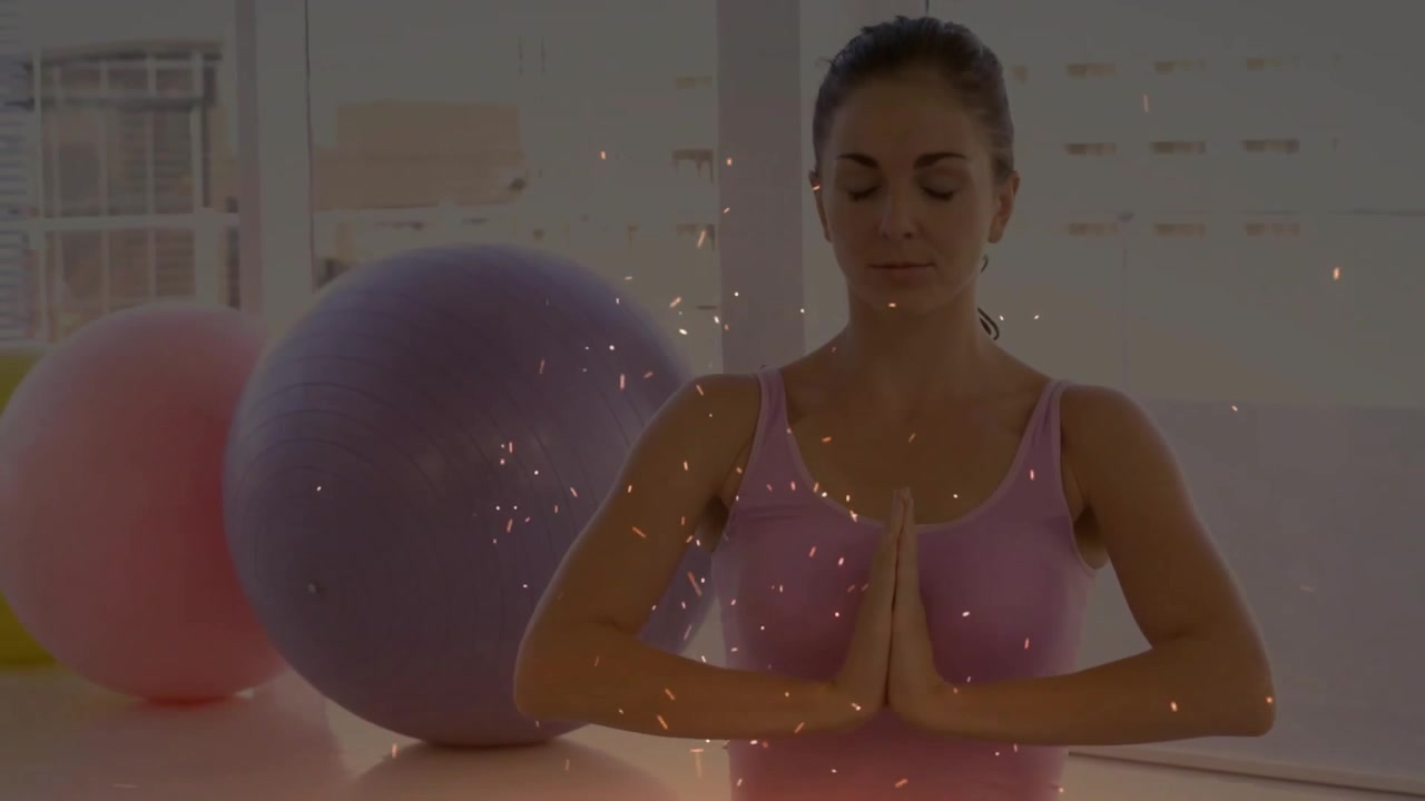 Donna seduta su tappetino yoga blu che solleva le braccia e inizia l'allenamento yoga con palloni da ginnastica colorati.
