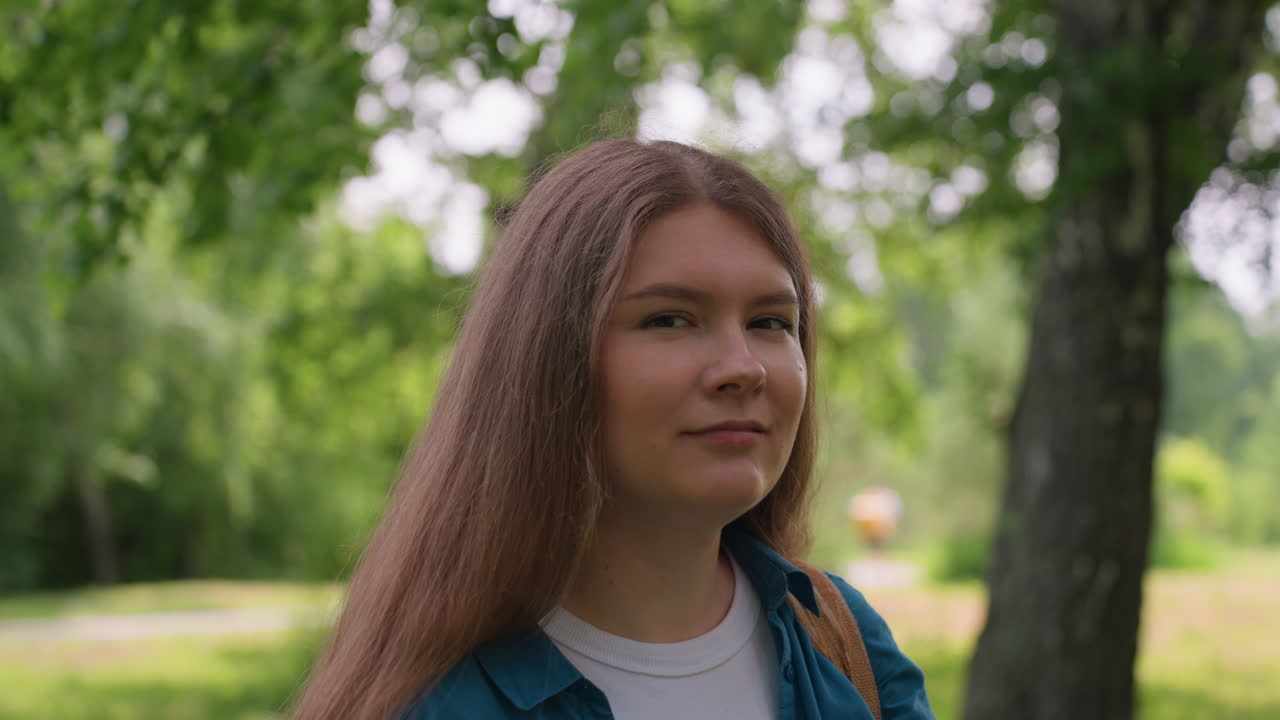 Lady removes sunglasses while enjoying peaceful moment in lush green park, feeling warm sunlight on face, wearing blue shirt and white top, showing calm relaxation