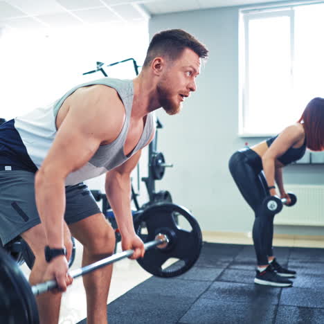 bearded athlete and healthy woman lifting heavy barbells in sport center. concentrated male and a female are doing the same exercise with barbell together in the gym.