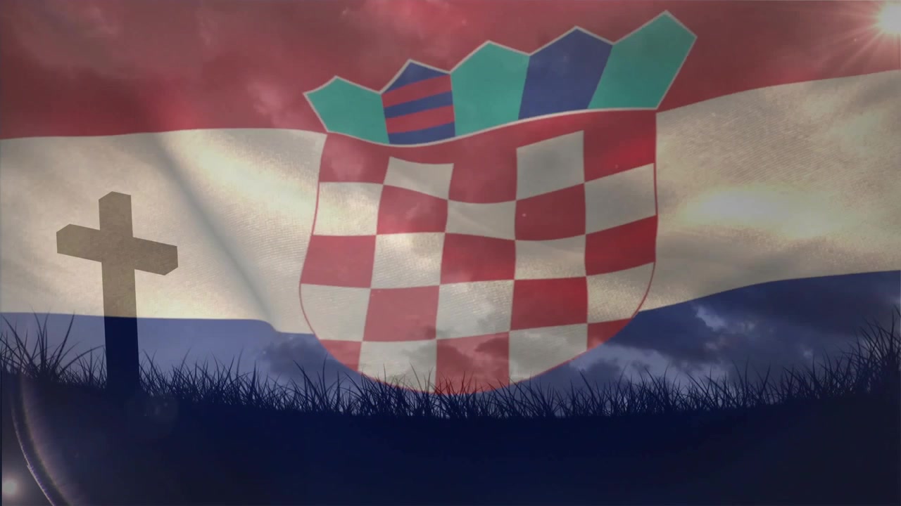 Eine wehende Flagge, die Brise verursacht Falten im karierten Schild und eine Sonnenreflexion verschiebt sich über einem Kreuzdenkmal.