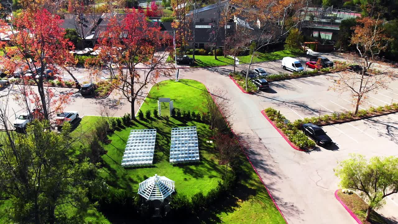 Aerial drone descending shot of an outdoor wedding venue with a gazebo and clubhouse in the background.