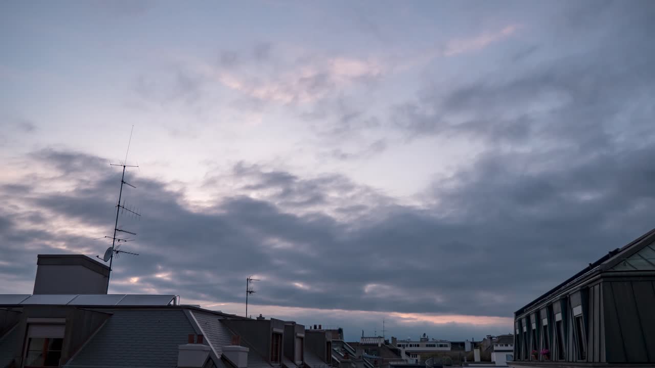 High clouds in sky moving on different atmospheric elevations and opposite directions above buildings, time lapse day to night