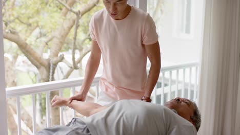 diverse male physiotherapist advising and senior male patient exercising on couch, in slow motion