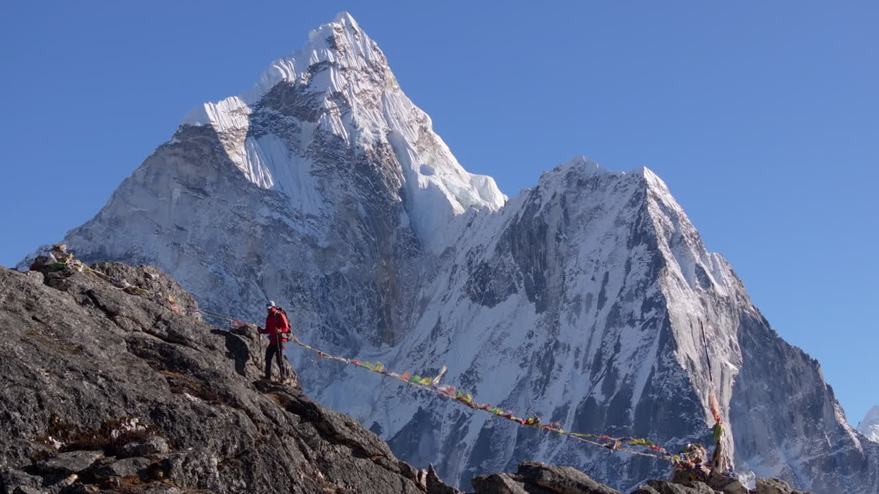 Foto aerea con teleobiettivo di un escursionista che si arrampica verso la vetta del Nangkartshang Peak vicino a Dingboche durante il trekking al campo base dell'Everest in Nepal. Ama Dablam e bandiere di preghiera sullo sfondo dell'Himalaya