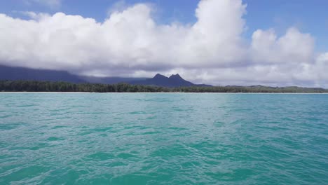 drone footage traveling across the breathtaking turquoise water of the pacific ocean heading toward the island of oahu in the hawaiian islands with purple mountains on the horizon