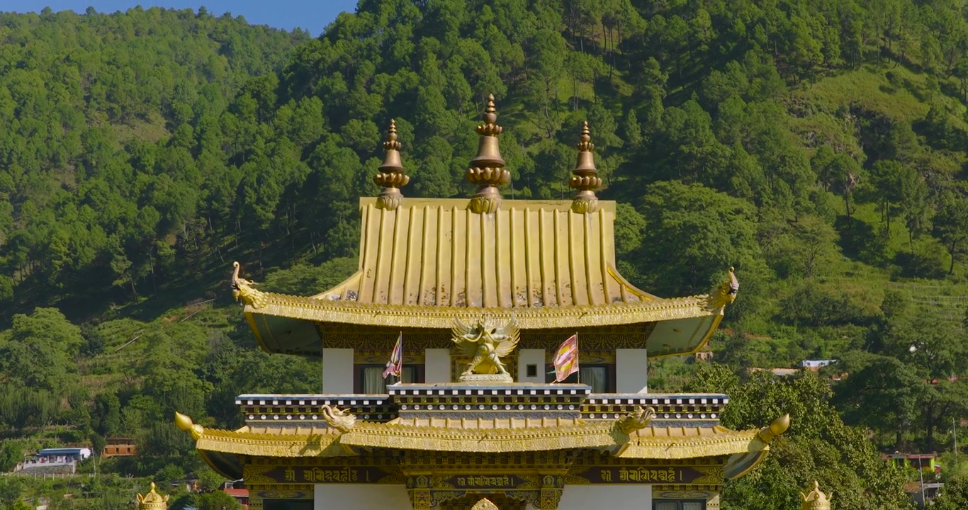 Droneoptagelse med nedefra-og-op-bevægelse og indzoomning af det gyldne tag på den buddhistiske klosterbygning i Pharping, Nepal, der viser den grønne bjergside i baggrunden