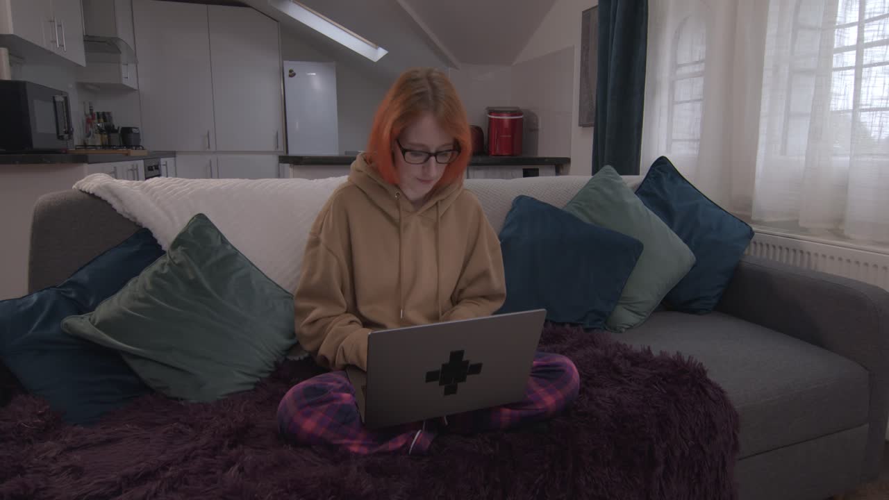 mujer remota trabajando en computadora portátil sentada en el sofá en casa en pjs