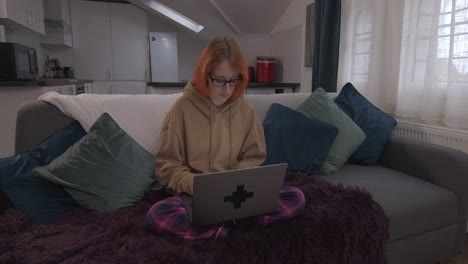 mujer remota trabajando en computadora portátil sentada en el sofá en casa en pjs