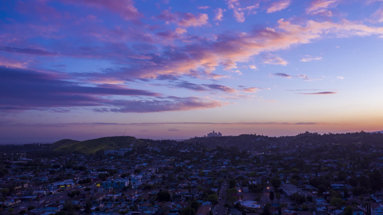 Dronová hyperlapse při západu slunce nad předměstím Los Angeles se siluetou centra města v dálce.