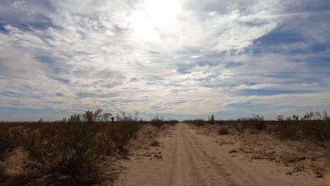 conductor pov conduciendo por un camino de tierra en el desierto de mojave hacia el cielo nublado