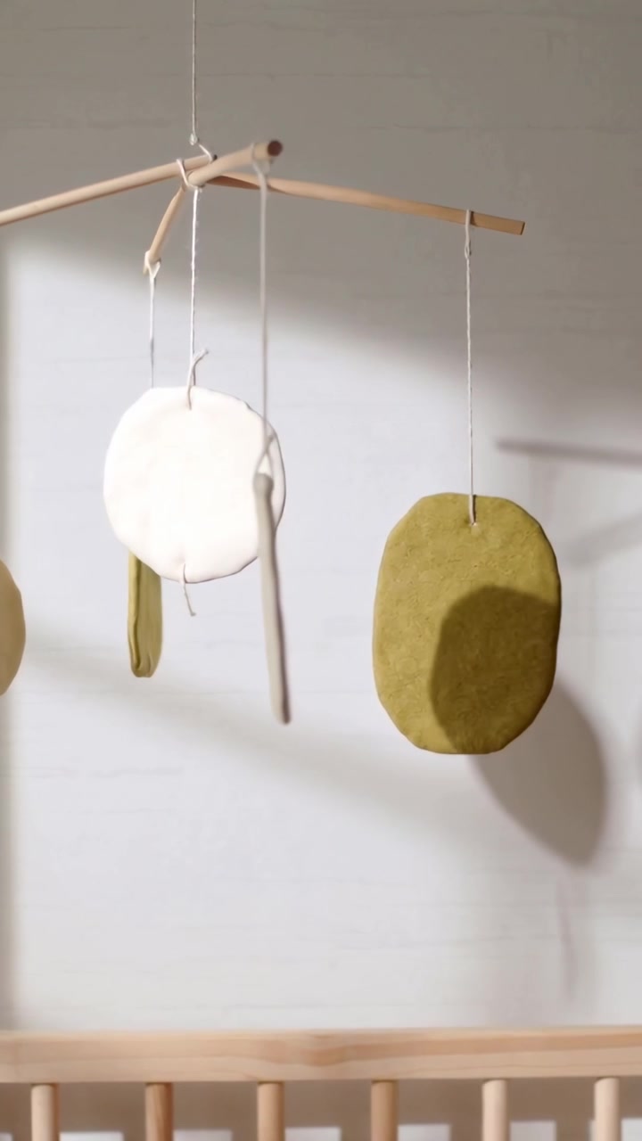 Video verticale: Mobile oscillante che ruota per una leggera brezza sopra una culla di legno, mostrando dischi d'oliva
