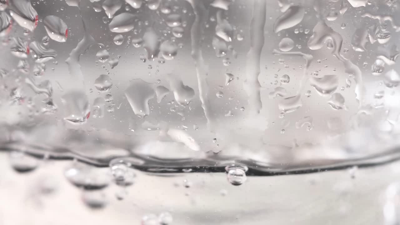 Observe droplets forming and merging on a transparent glass surface, showcasing surface tension and fluid dynamics.