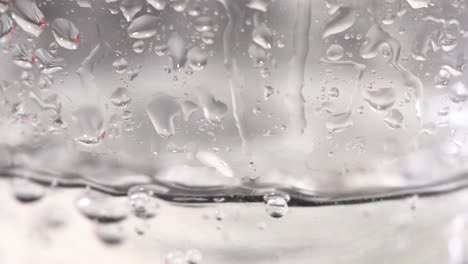 observe droplets forming and merging on a transparent glass surface, showcasing surface tension and fluid dynamics.