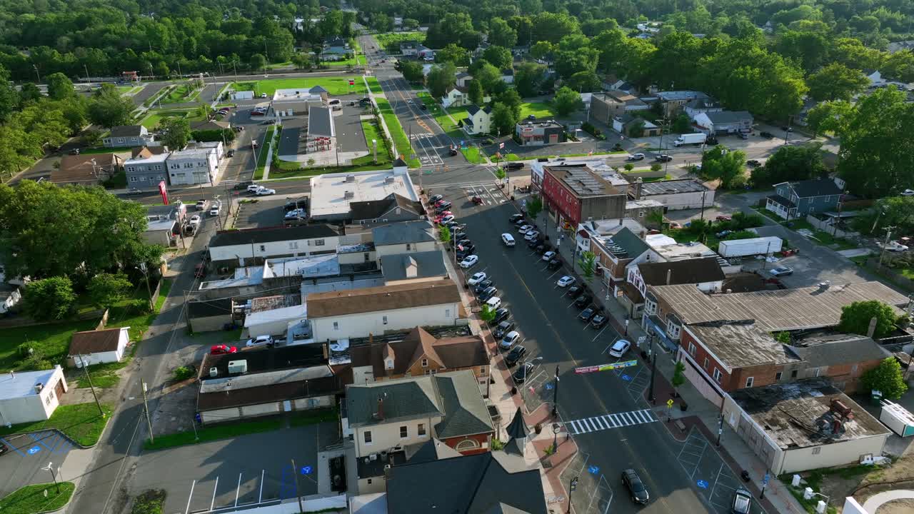 Traffic on Main Street and junction of historic town in summer. Descend drone top down. Green trees lighting at sunset. Marketplace and stores in historic row buildings. Wide shot