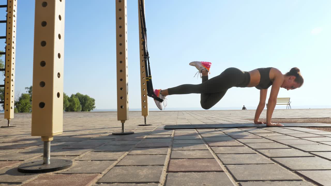 entrenamiento al aire libre. correas de suspensión. entrenamiento con correas. mujer joven atlética está haciendo ejercicios de resistencia de todo el cuerpo usando cuerdas en bucle trx, en la playa durante la puesta o el amanecer. entrenamiento de fitness al aire abierto. concepto de estilo de vida saludable. deporte matutino