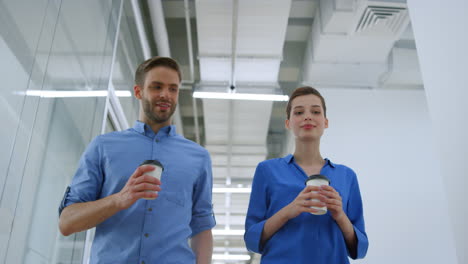 Colleagues-walking-with-paper-cups-in-office.-Business-woman-and-man-talking