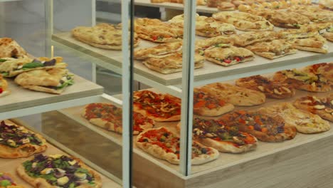 counter full of pizzas and focaccias with delicious toppings on display in a pizzeria, italy.