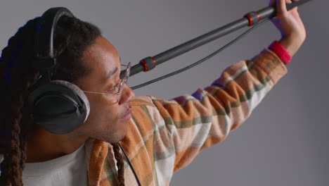 male film sound recordist wearing headphones holding microphone boom pole above actor shooting movie or video in studio 2