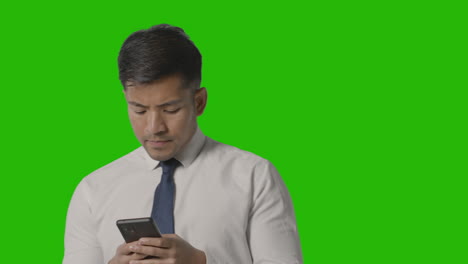 foto de estudio de un hombre de negocios con camisa y corbata pensando usando un teléfono móvil contra una pantalla verde