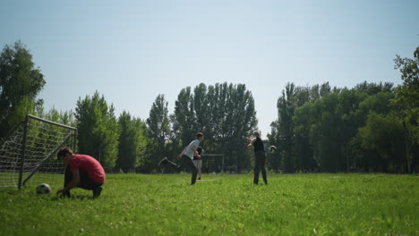 a grandfather and grandson play football, the grandfather throws, the grandson heads the ball, nearby, someone ties his shoelace near a goalpost