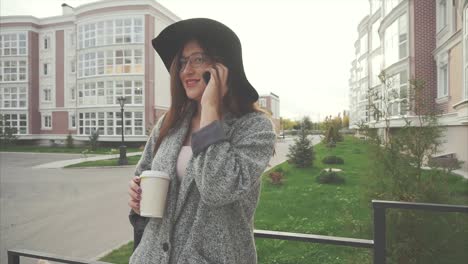 mujer en una llamada telefónica, disfrutando de un café fuera de un edificio de apartamentos