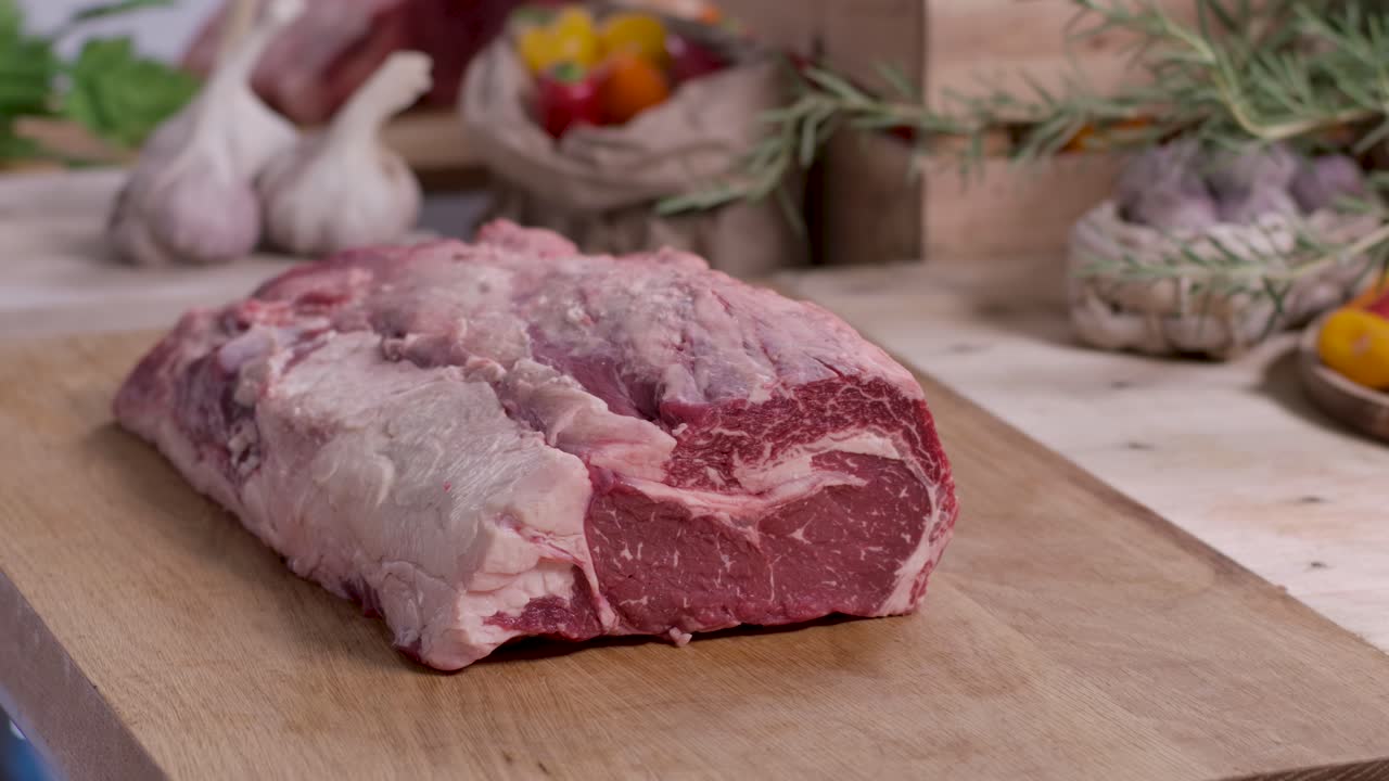 Close up of a professional butcher's hands placing a large, prime marbled raw beef roast onto a rustic wooden cutting board in a kitchen setting
