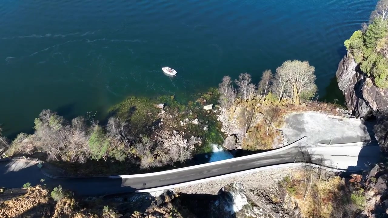 Drone si tuffa oltre il bordo di una cascata verso una strada e una barca in un fiordo norvegese vicino a Stamnes, Norvegia