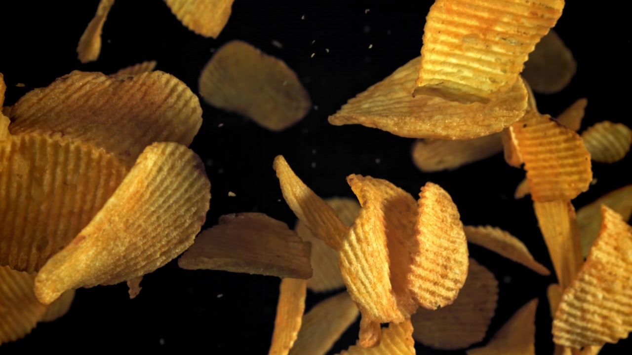 Golden Ruffled Potato Chips Falling in Slow Motion on Black Background