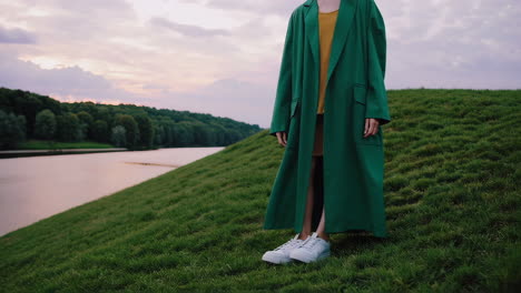 person in green coat and white sneakers on a grassy hill