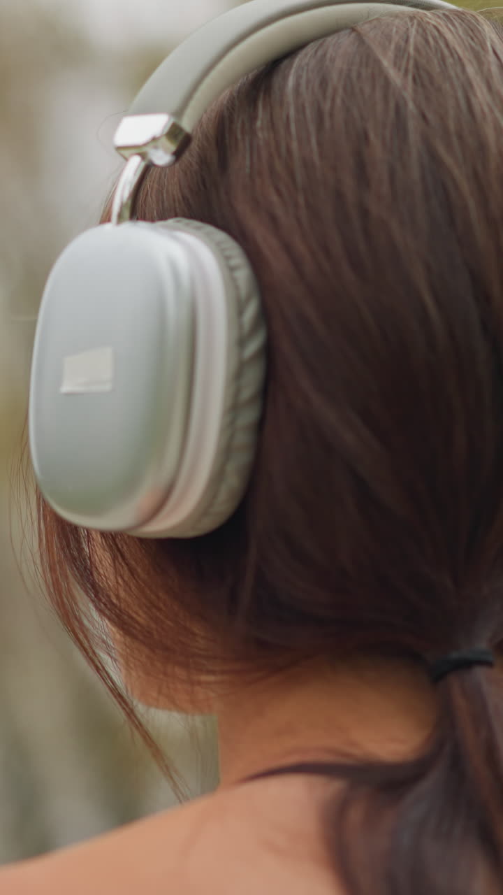 Back view of young girl wearing headphones with a wristwatch on her hand, looking relaxed and connected with nature, capturing a peaceful moment while enjoying music outdoors
