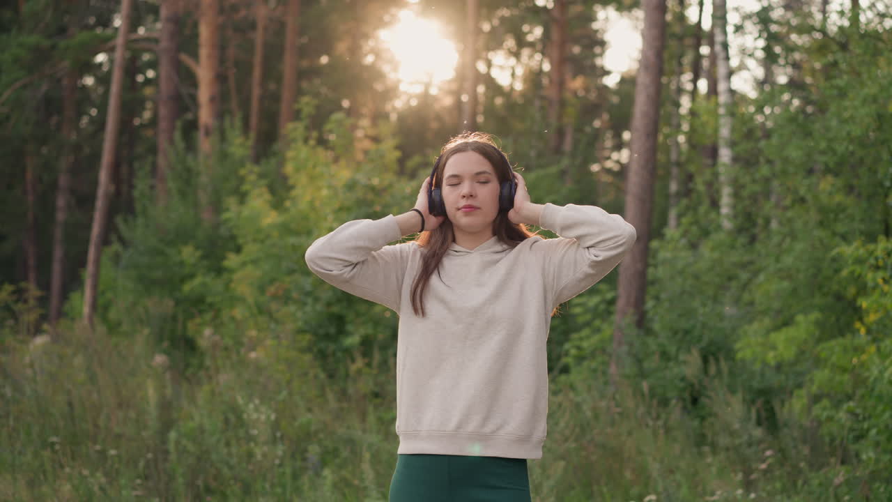 dama con auriculares se encuentra en el bosque. mujer joven con cabello largo y suelto saborea los ritmos de la música de relajación en el aire fresco al atardecer. relajación por la noche
