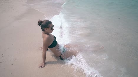 waves wash woman body lying on beach in black swimsuit