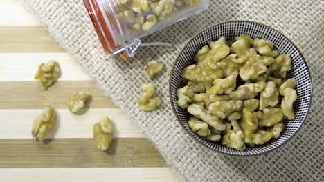 Panning-shot-birds-eye-across-bowl-full-of-walnuts-set-on-hessian-cloth-striped-wooden-table