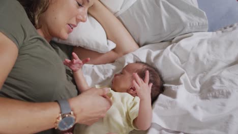 Video-of-happy-caucasian-mother-playing-on-bed-with-newborn-baby