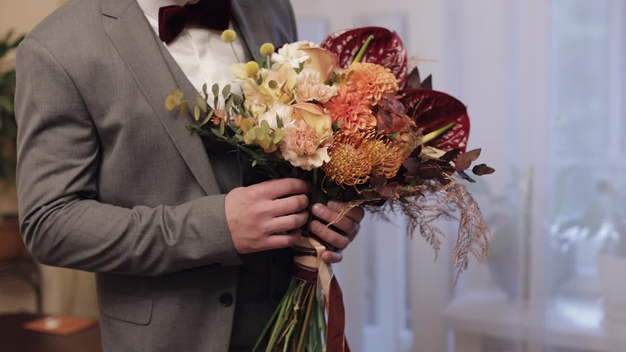Sposo con bouquet nuziale tra le mani a casa, che si prepara ad andare dalla sposa, primo piano, slow motion.