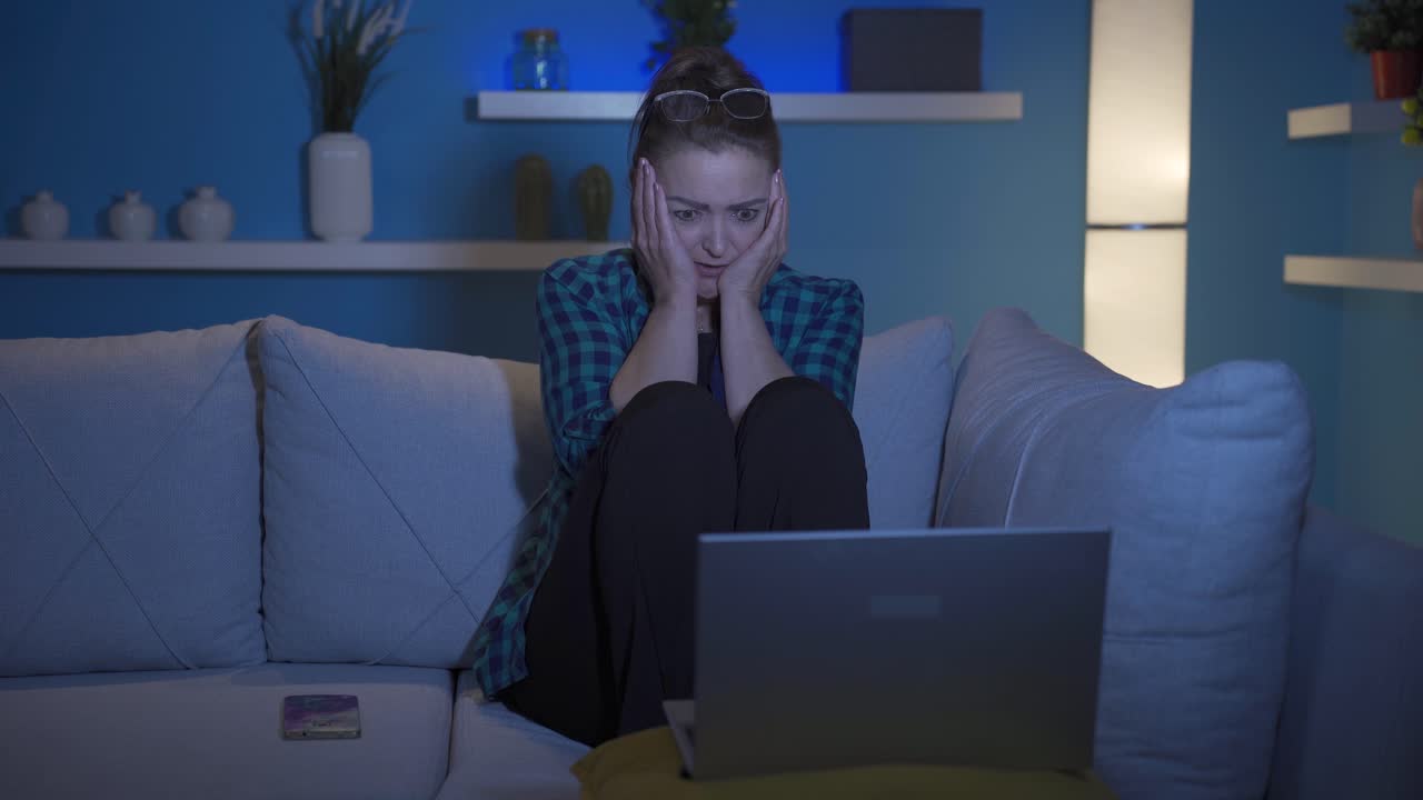 mujer viendo una película de terror en el portátil por la noche. la mujer está asustada y tensa.