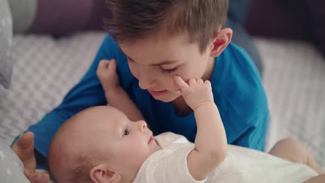 siblings have fun on bed. boy playing with baby. older brother care infant