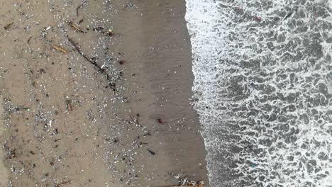 slow motion aerial shot as waves washing out garbage from the sea, polluted ocean coast