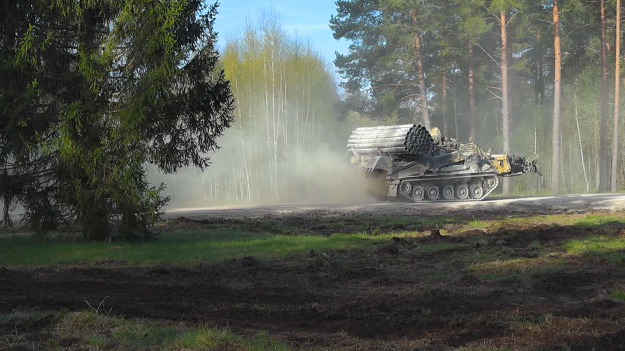 Rare slow motion footage of a British trojan or a engineering Challenger 2 4034 tank driving by on a rural countryside dusty white road in the middle of a pine forest and green grassy field, sunny day