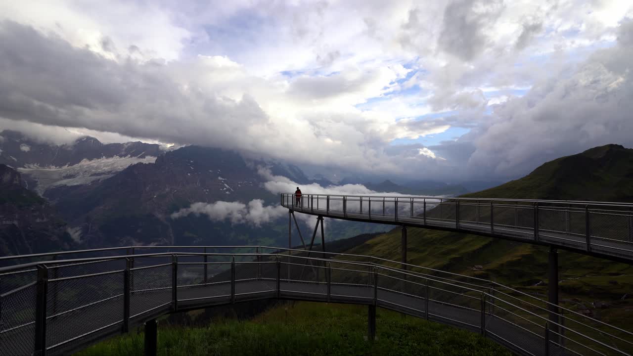 persona en una plataforma de observación de montaña con cielos nublados y telón de fondo alpino, luz del día